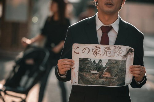 スーツ姿の男性が古い写真付き怪文書を掲げる街角の光景