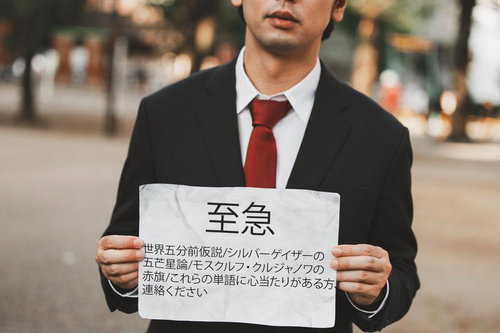 至急と書かれた怪文書を持つ黒いスーツの男性