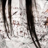 意味不明な文字が書かれた怪文書を握りしめる長髪女性の手元の写真