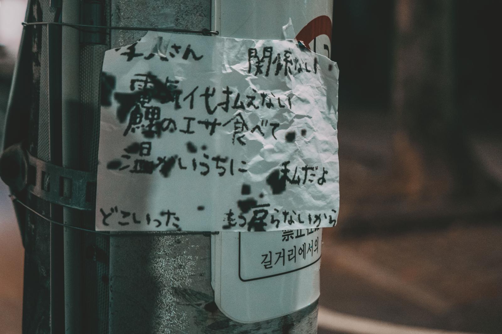 電柱に貼られた手書きの文字が書かれた白い紙と韓国語ステッカー