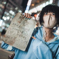 白マスク姿で怪文書を掲げる青いパーカーの女性の写真