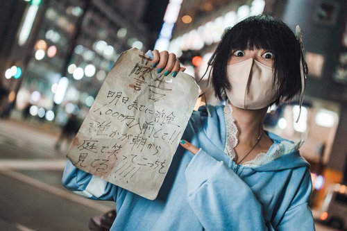 白マスク姿で怪文書を掲げる青いパーカーの女性