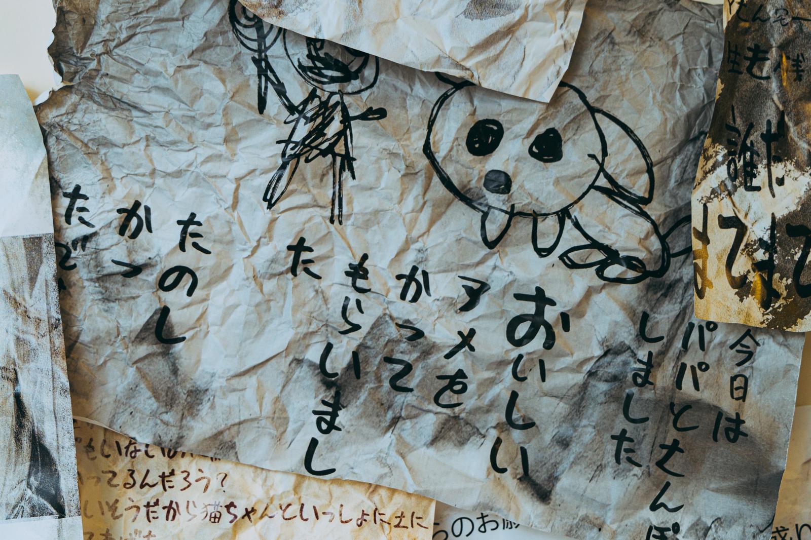 シワシワに折れた古い紙に黒いペンで描かれた子どもの落書きと断片的な文字