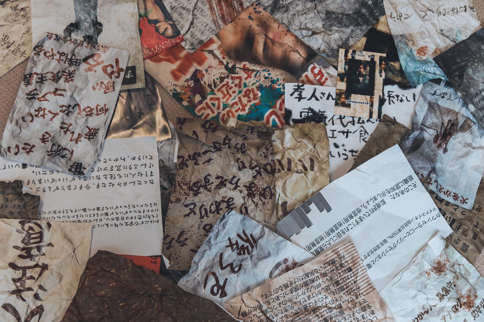 Old paper fragments with handwritten characters and mysterious documents (kaibun) scattered on floor, with creases and stains