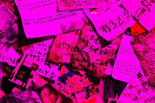 ピンク照明で照らされた大量の紙片と文字が散乱する光景