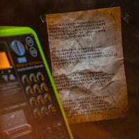 緑色の公衆電話と手書きの怪文書が置かれた薄暗い空間の写真