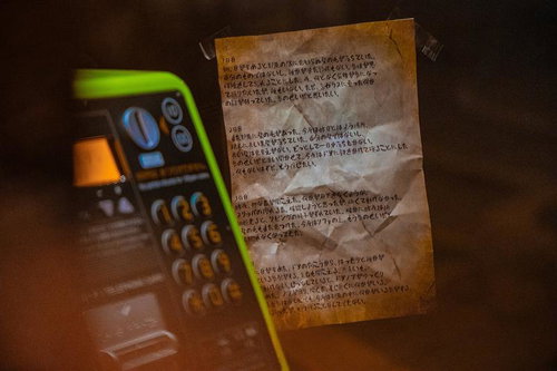 緑色の公衆電話と手書きの怪文書が置かれた薄暗い空間