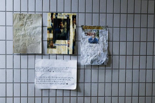 白いタイル壁に貼られた手書き文書と写真の掲示物