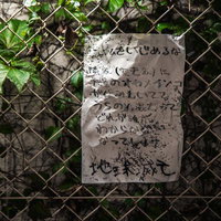 金網フェンスに貼られた汚れた手書きの怪文書の写真