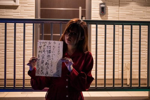 住宅街の手すりに座り怪文書を掲げる赤い服の女性