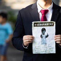 黒いスーツの男性が怪文書を掲げる不気味なシーンの写真
