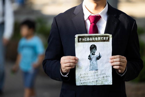 黒いスーツの男性が怪文書を掲げる不気味なシーン