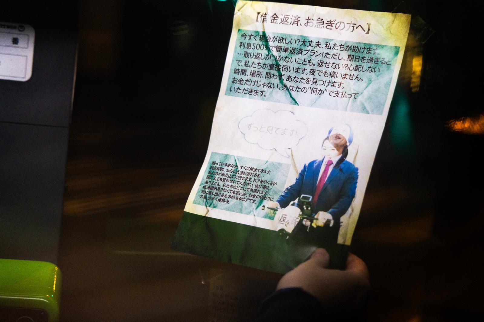 夜道で受け取った闇金業者を装う怪文書のビラを手に持つ場面