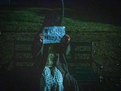 夜のベンチで怪文書を掲げる謎の女性