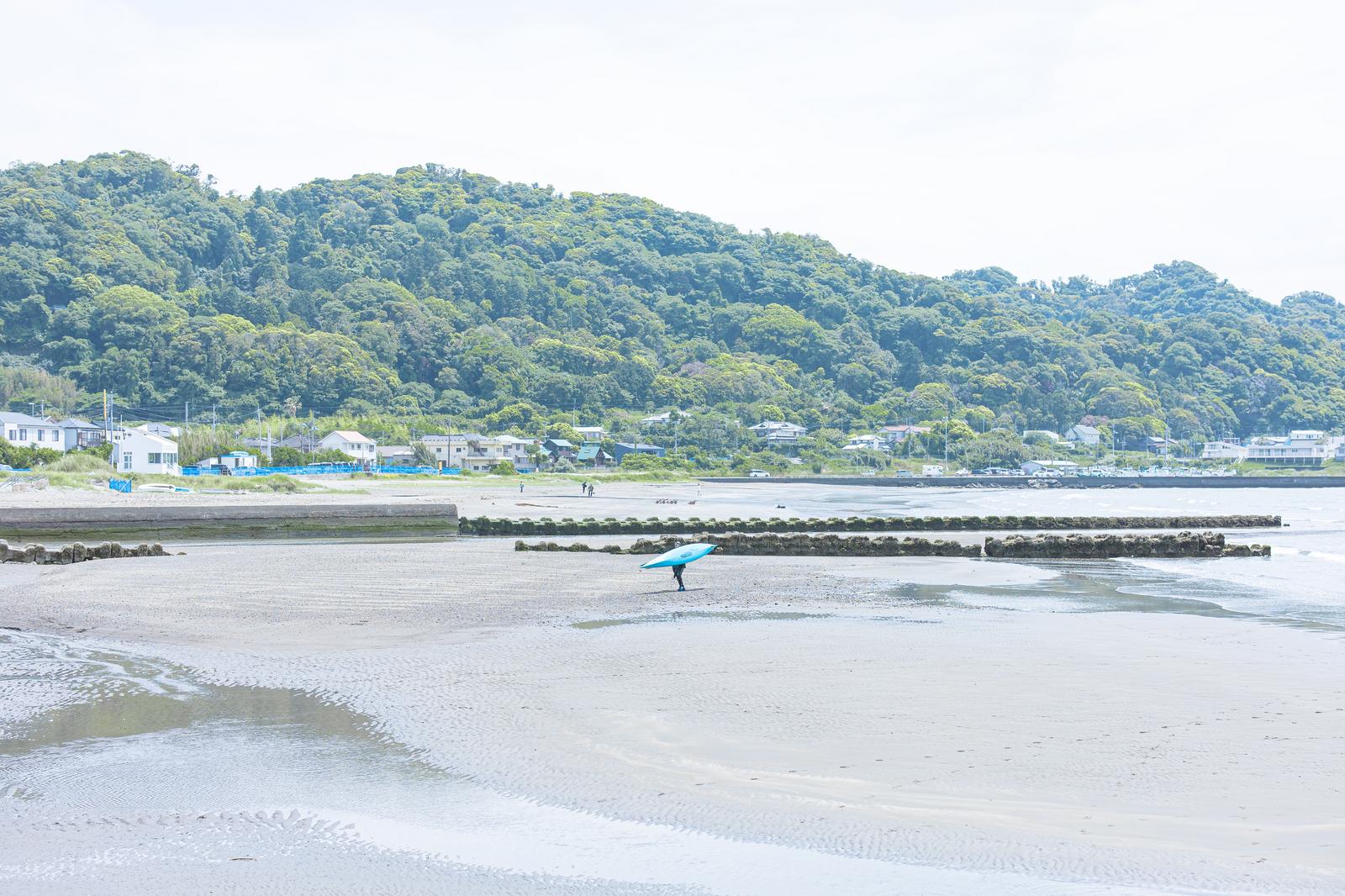 岩井海岸で青いサーフボードを持つ人が波打ち際に立っている