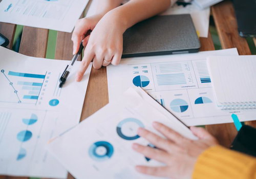 紙の資料を広げて議論する会議風景、グラフとデータ分析