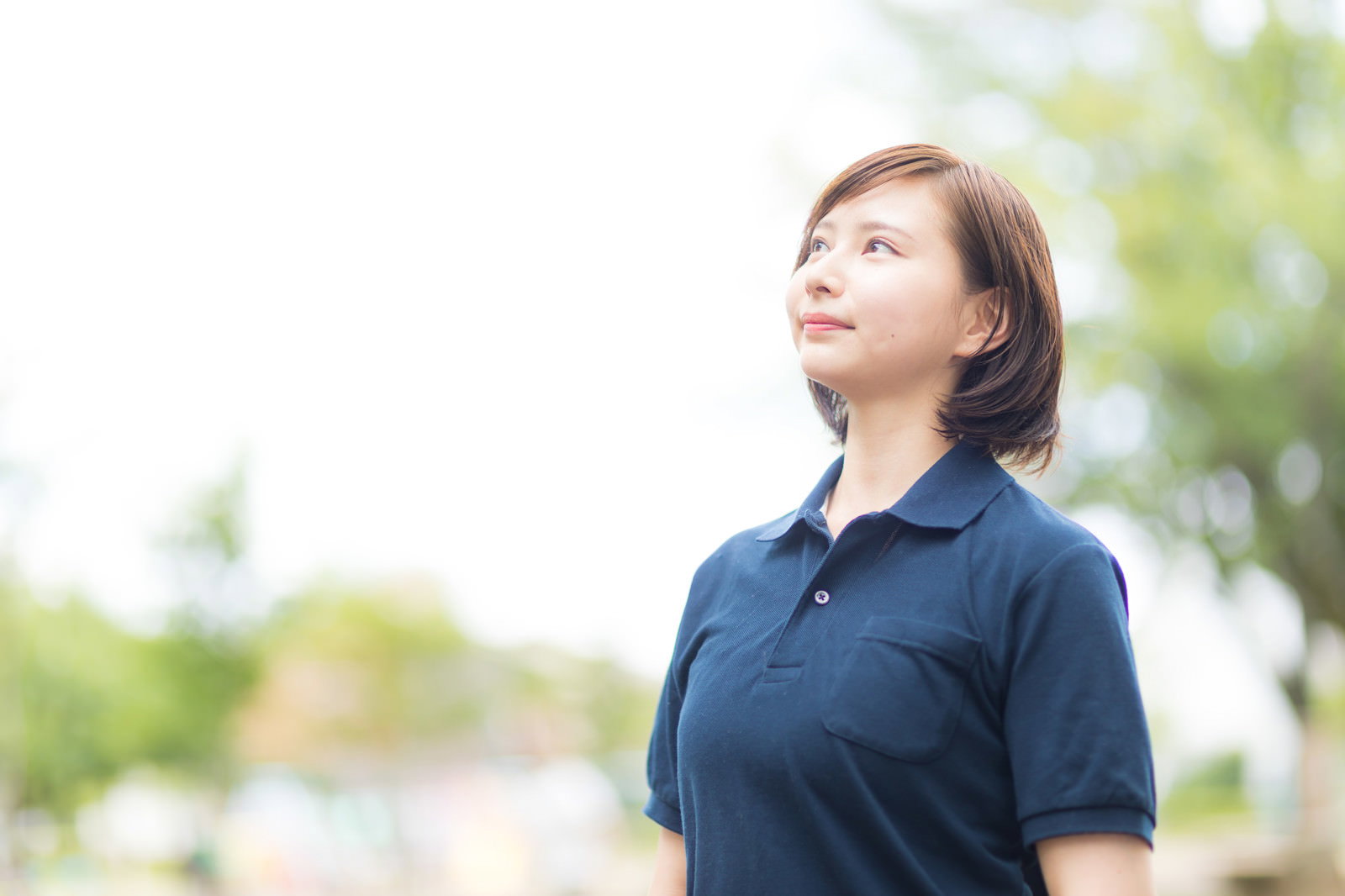 紺色の制服を着たヘルパーの女性が屋外で空を見上げている様子［モデル：yumiko］
