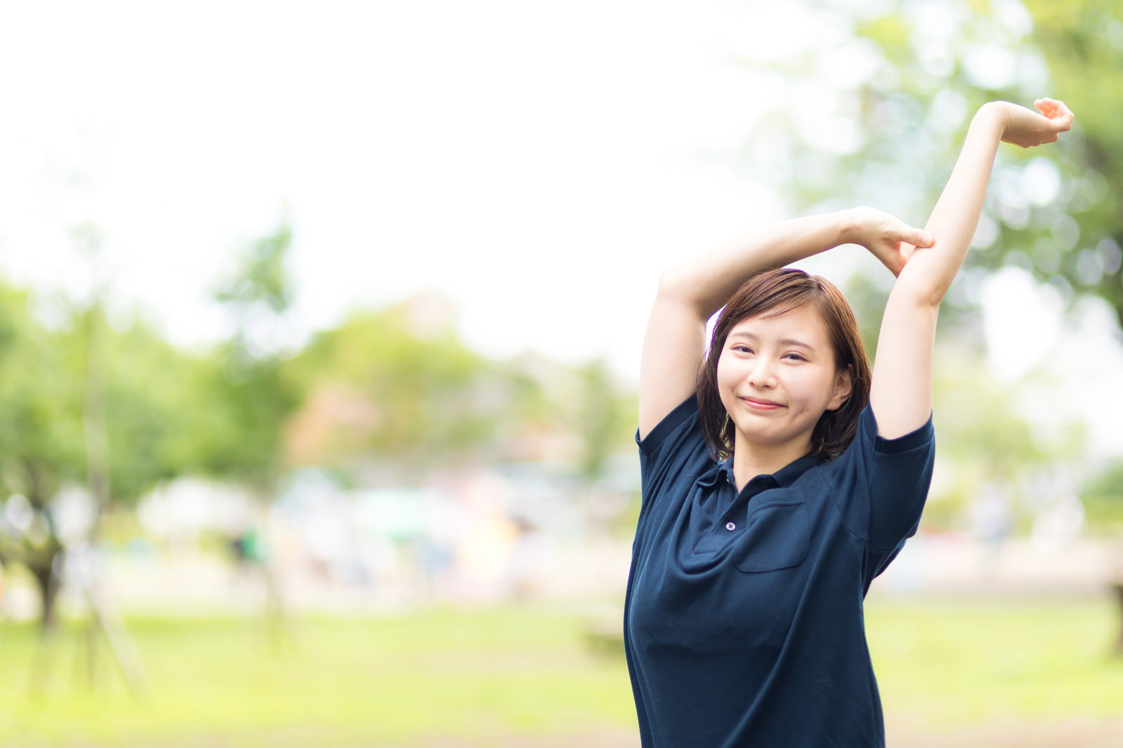 公園の緑の中で両手を上げて伸びをしている女性［モデル：yumiko］