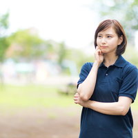 公園で頬に手を当てて考え込むヘルパーの女性の写真