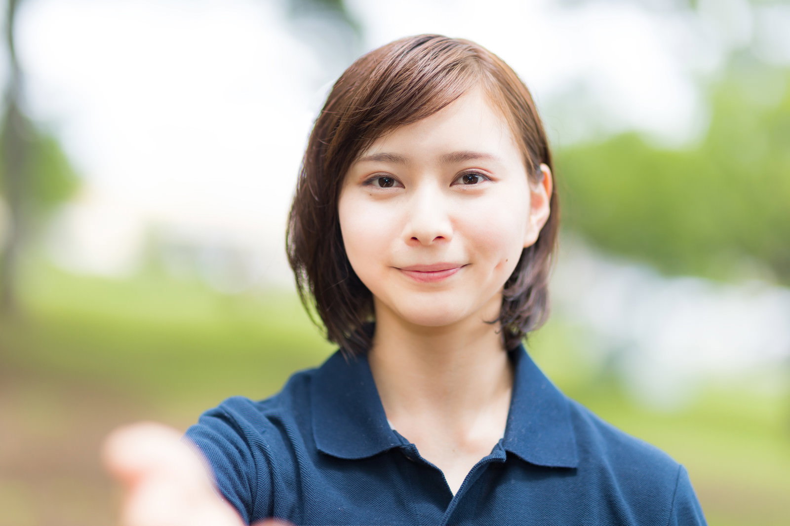 紺色のエプロンを着た女性ヘルパーが両手を差し伸べている様子［モデル：yumiko］