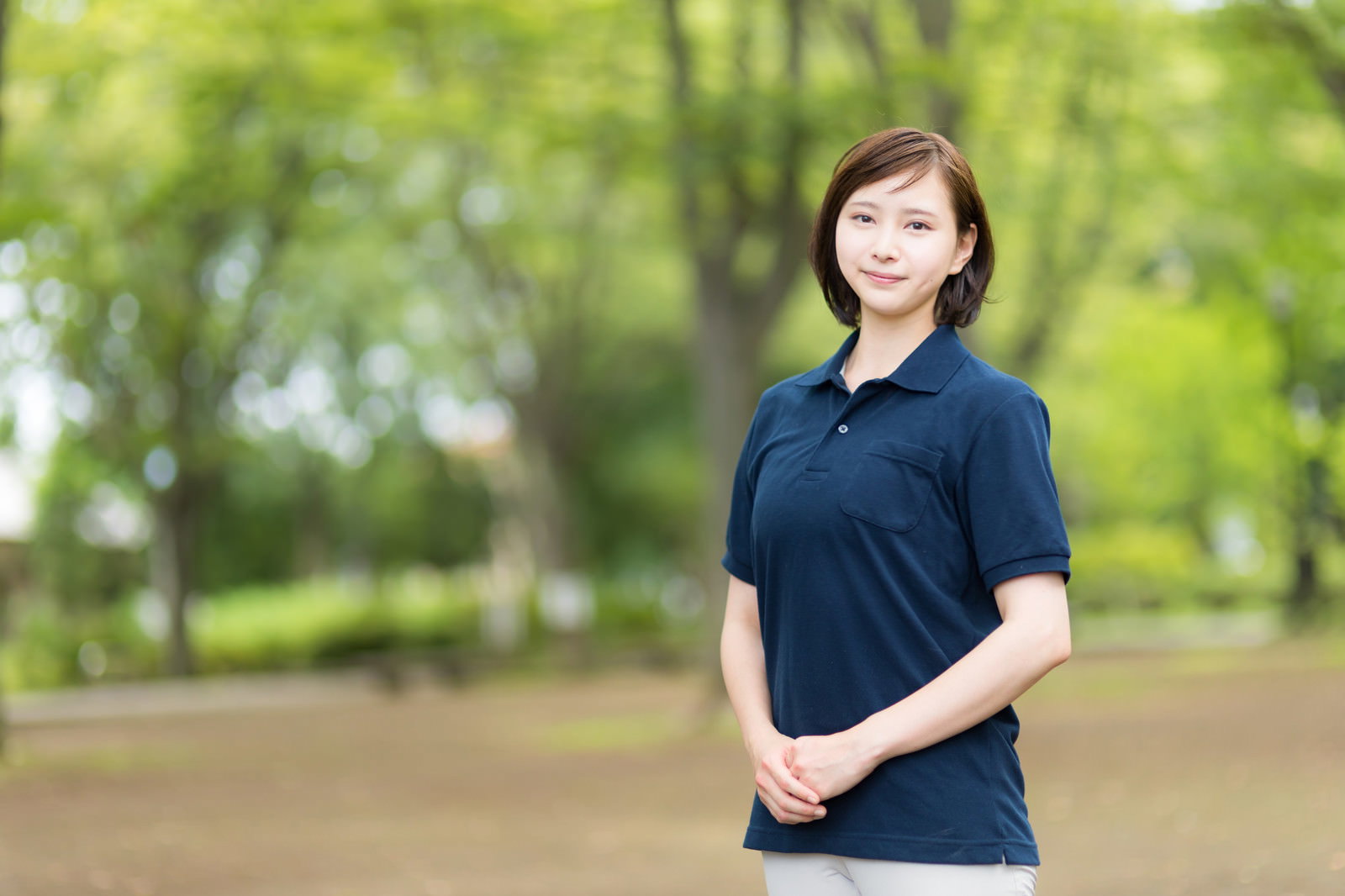 新緑の公園で紺色の制服を着て笑顔を見せる介護士の女性［モデル：yumiko］