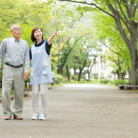 新緑の公園で笑顔で散歩するお爺さんと介護士の様子の写真