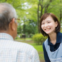公園でお爺さんの昔話を笑顔で聞く介護士の女性の写真