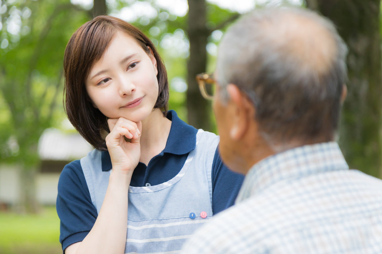 公園で頑固な高齢男性と会話する困った表情の女性介護士［モデル：yumiko まーちゃん］