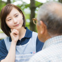 公園のベンチで頑固な老人と対話する介護士の女性の写真
