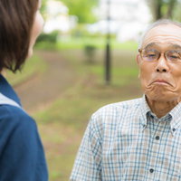 口をへの字にして動かない高齢者と説得するヘルパーの写真