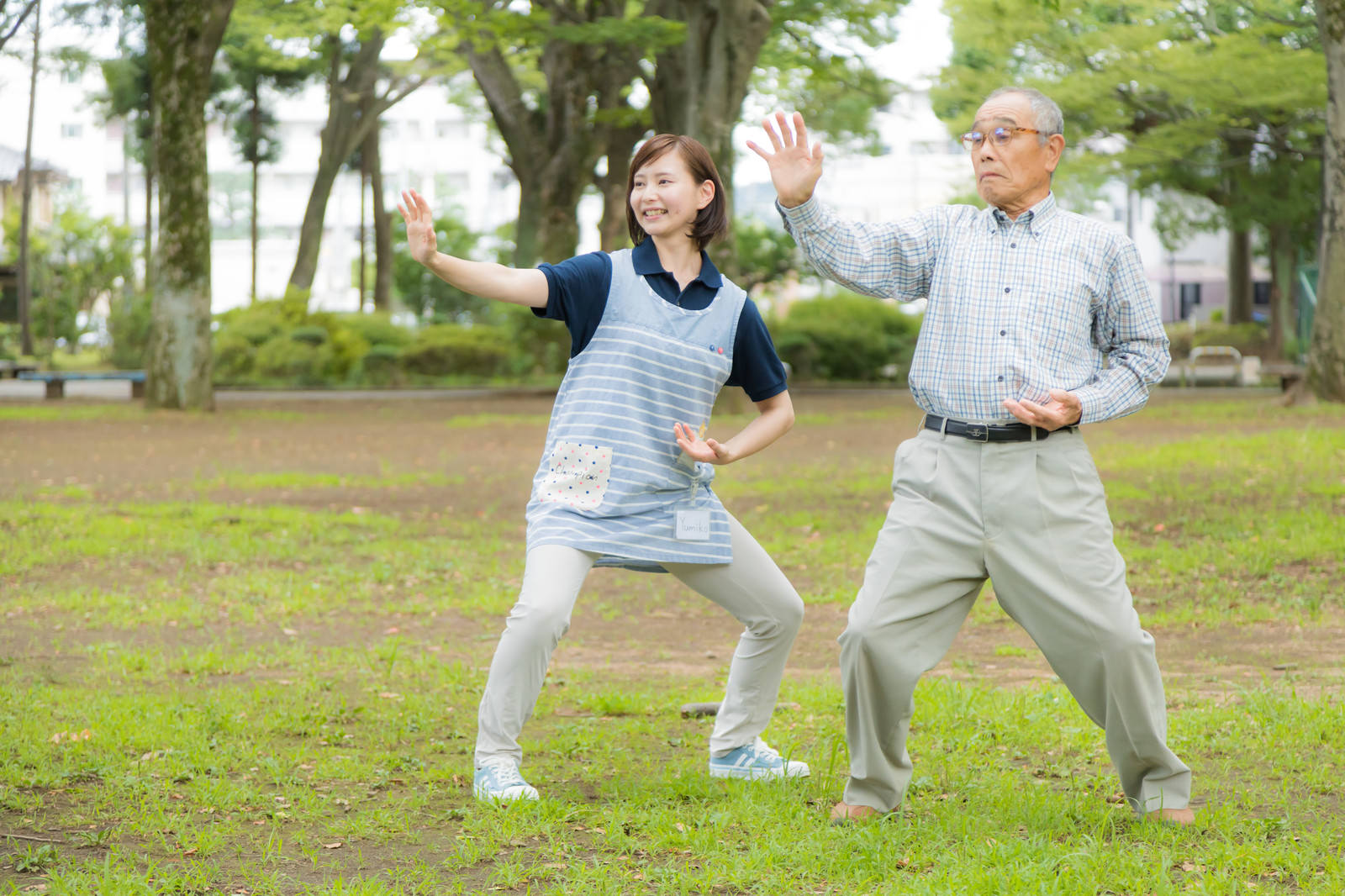 公園で太極拳のような体操をする高齢男性と付き添う介護士女性［モデル：まーちゃん yumiko］
