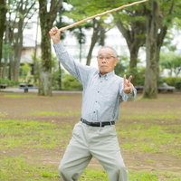 公園で棒を振りかざしてポーズを決めるお爺さんの写真