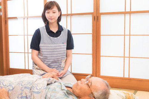 寝たきりのお爺さんを心配する介護士の女性