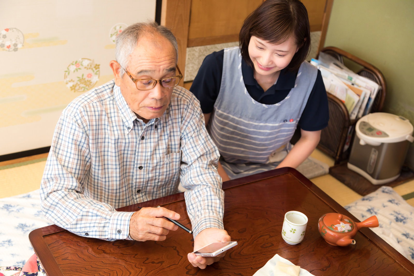 スマートフォンでビデオチャットを楽しむ高齢男性と横で見守る女性介護士