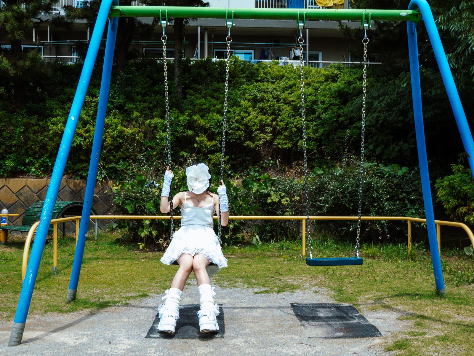 公園のブランコに座る白いロリータ服の人物［モデル：田村未完］