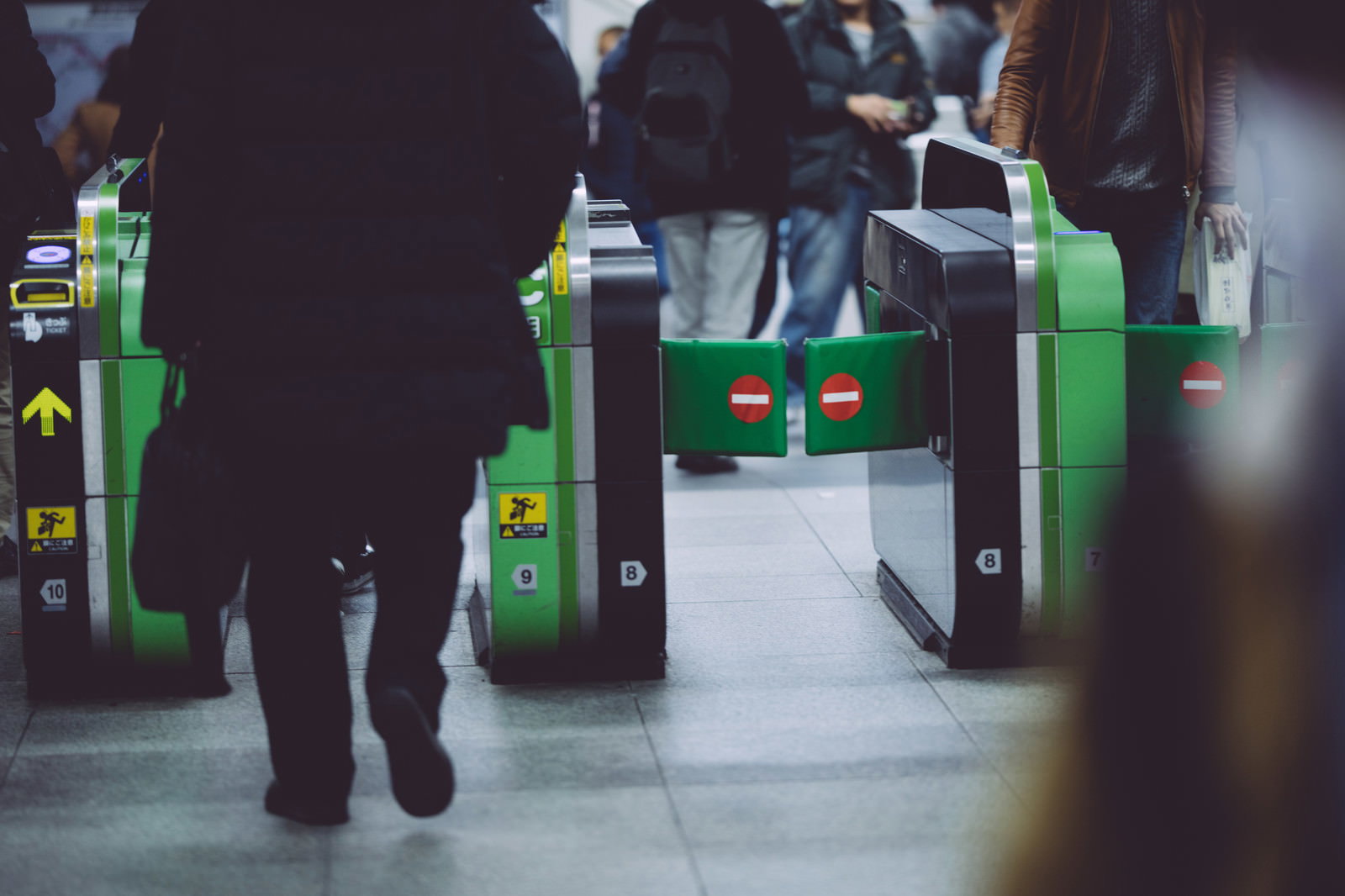 緑色の改札機を通過する会社員の足元を捉えた駅構内の様子