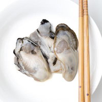 箸で取る皿に盛り付けた牡蠣の身、竹製の取り箸が添えられた白い皿の写真