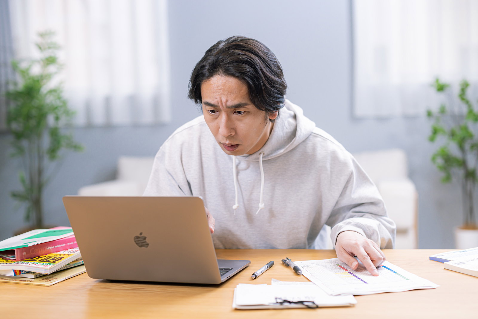 ノートパソコンと書類を前に、困った表情で確定申告書類を確認する男性［モデル：大川竜弥］