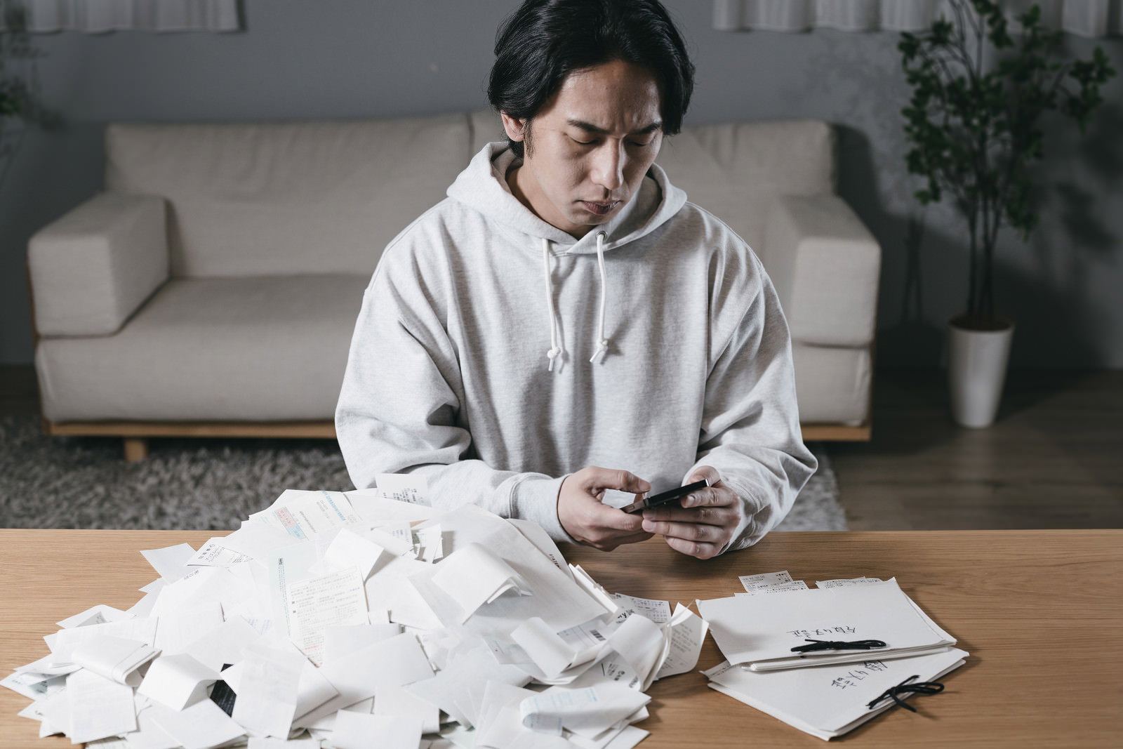 領収書に囲まれながらスマートフォンを操作する男性［モデル：大川竜弥］