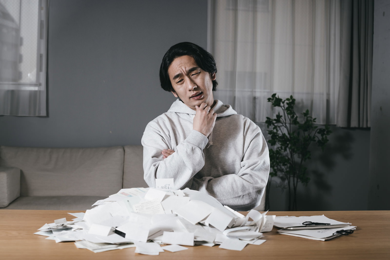散らばった領収書を前に手を当てて考え込む男性［モデル：大川竜弥］