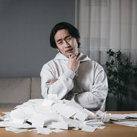 散らばった領収書を前に考え込む男性の確定申告業務の写真