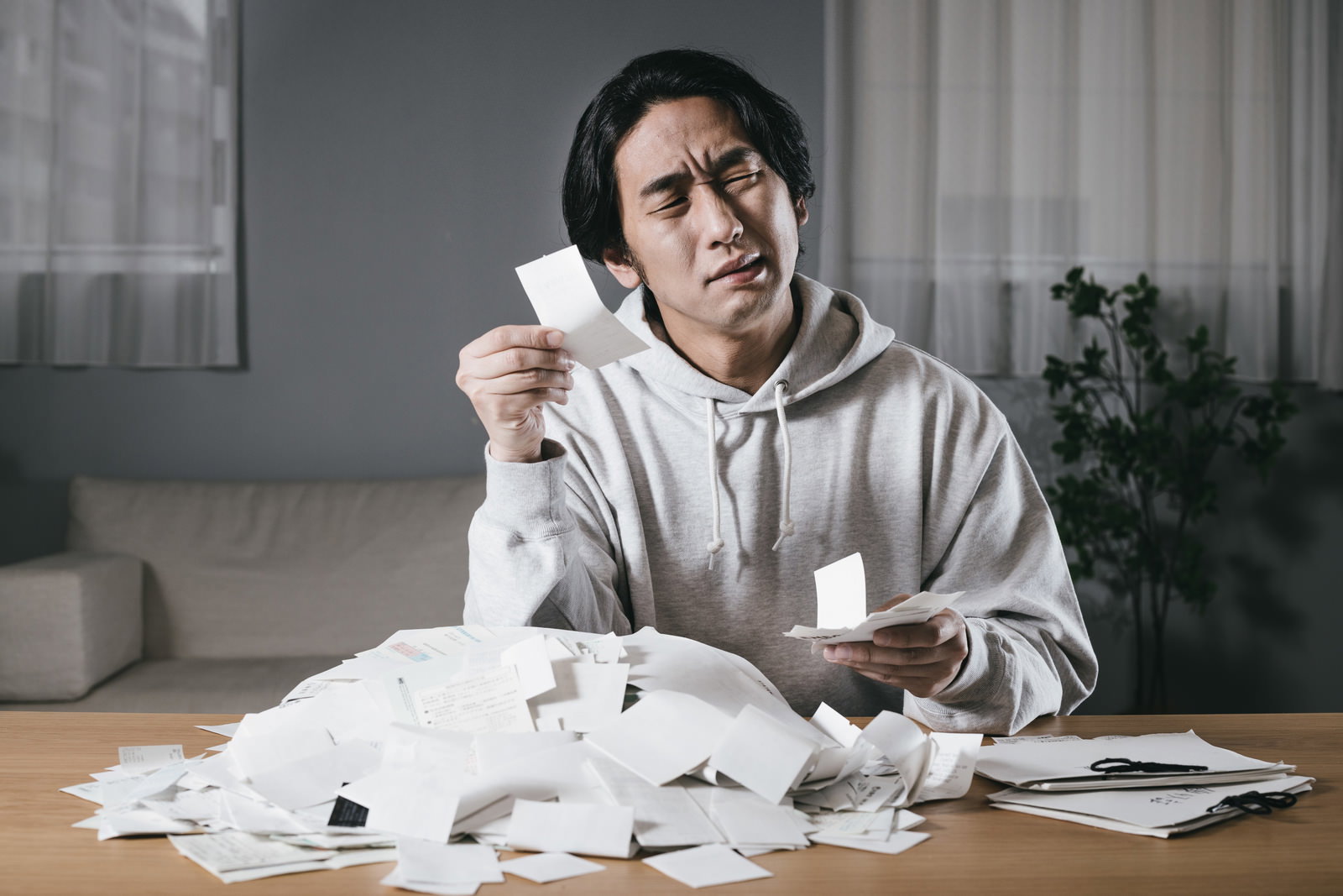 領収書を持ちながら困惑した表情で目を閉じる男性［モデル：大川竜弥］