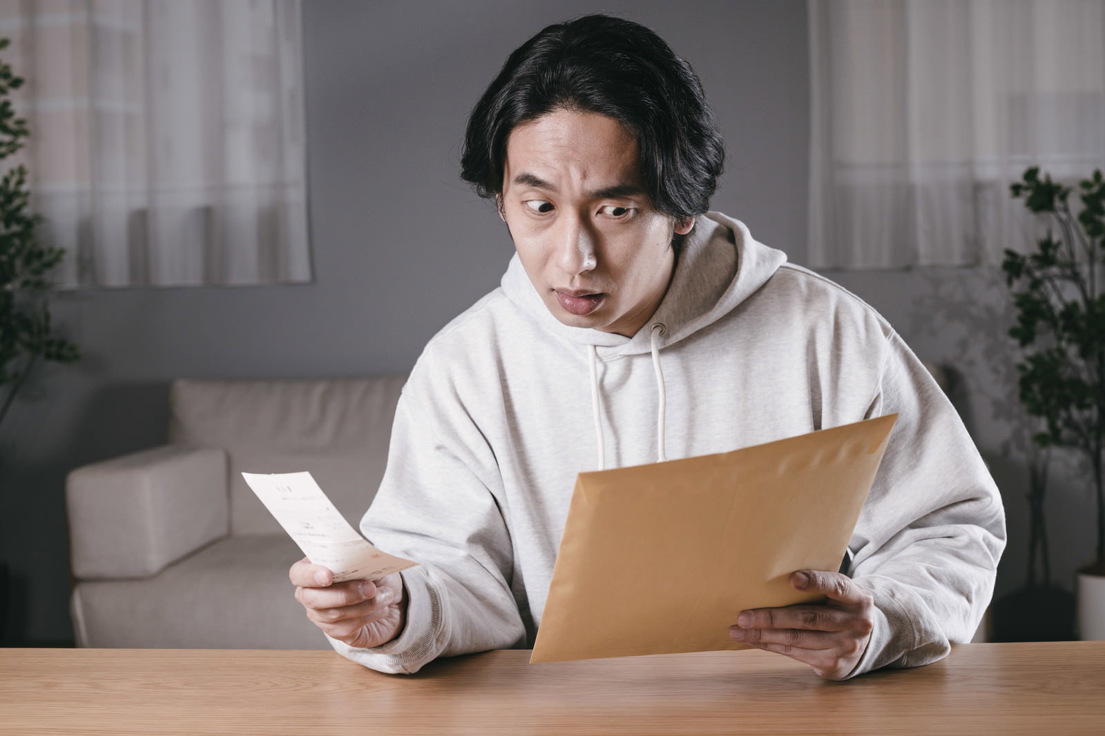 白いパーカーを着た男性が、閉じた封筒と書類を見て唖然とした表情をしている［モデル：大川竜弥］