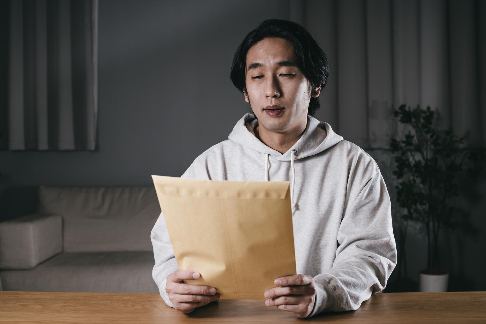 グレーのパーカーを着た男性が茶色い封筒を持ち、不安そうな表情で見つめている写真［モデル：大川竜弥］