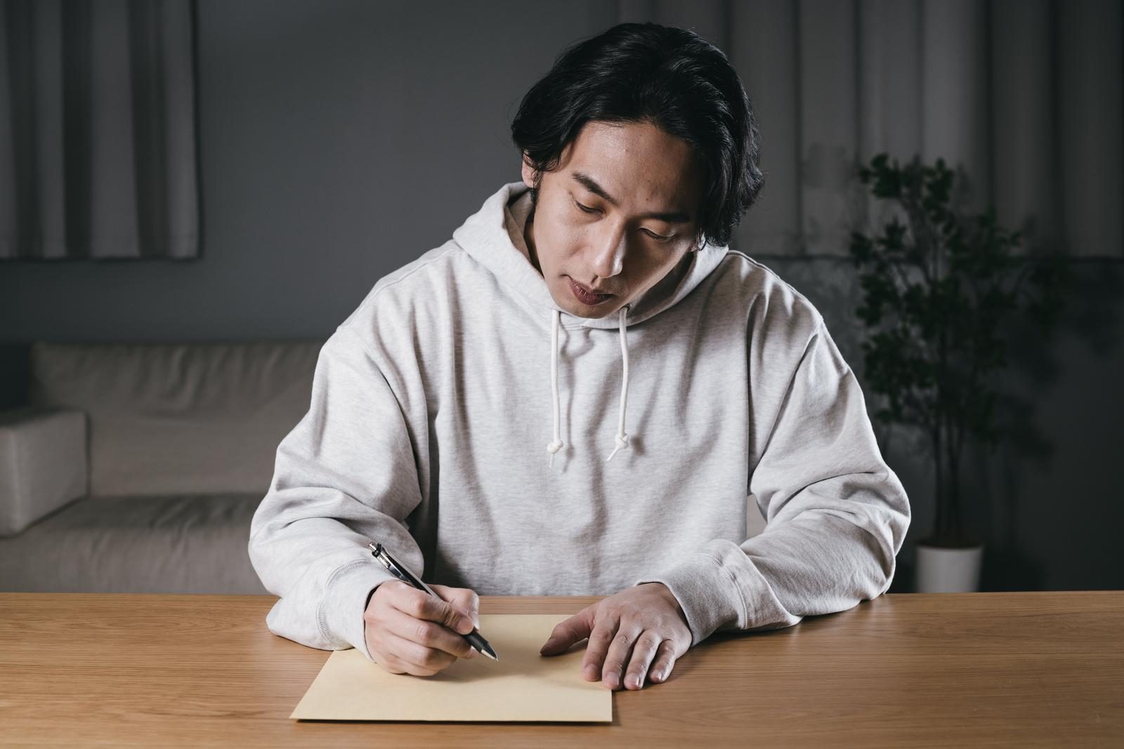 封筒に宛先を書き込む男性が机に向かっている［モデル：大川竜弥］