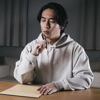 送り先の住所が思い出せず封筒を前に考える男性の写真