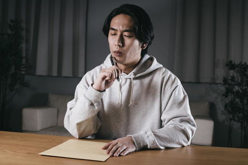 送り先の住所が思い出せず封筒を前に考える男性