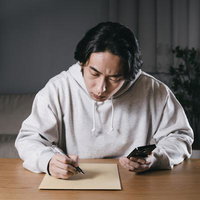 夜な夜な宛先をスマートフォンで確認しながら手書きする個人事業者の写真