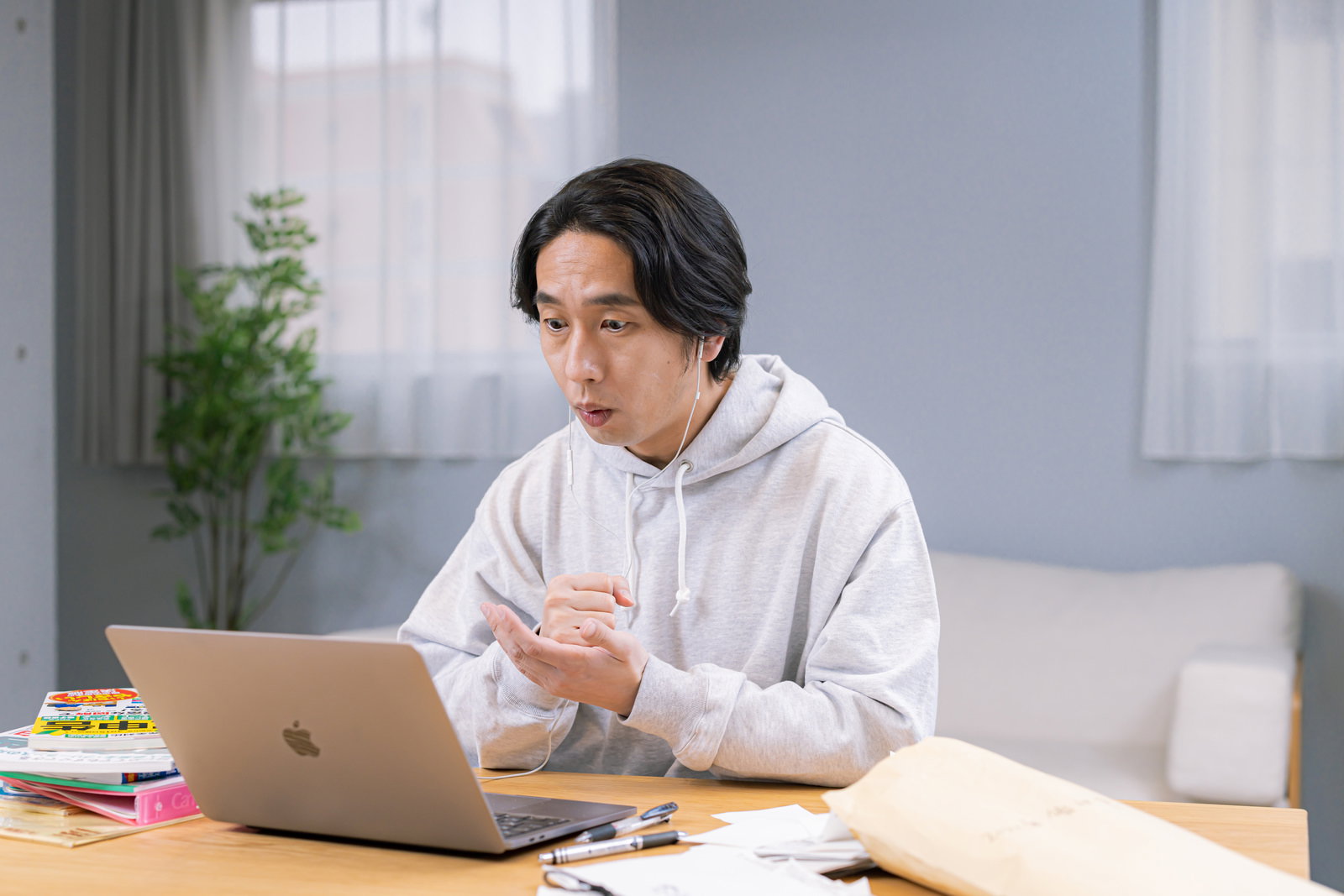 ノートパソコンを前に納得した様子でジェスチャーする男性と、テーブル上の書類・ファイル［モデル：大川竜弥］