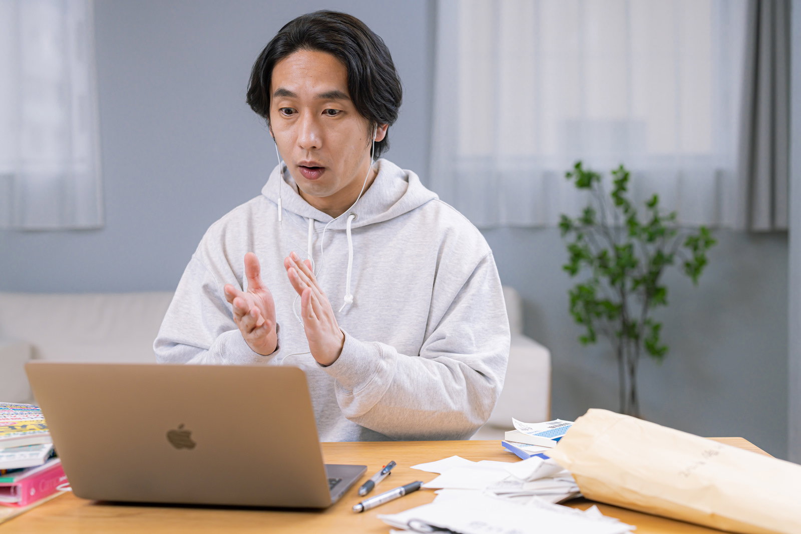 ノートパソコンを見ながら両手を打ち合わせる白いパーカーの男性［モデル：大川竜弥］